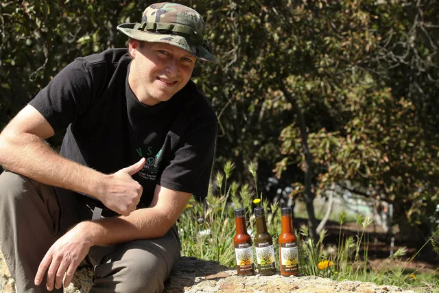Mike N. Hanes, chief executive officer of Forger Mike Superfoods, poses for a photograph next to three bottles of his lastest success; "DANG !!! it's good hot sauce," at Archis Acres, March 7. Sauce making mistakes: the stage ladder from bench to shelf